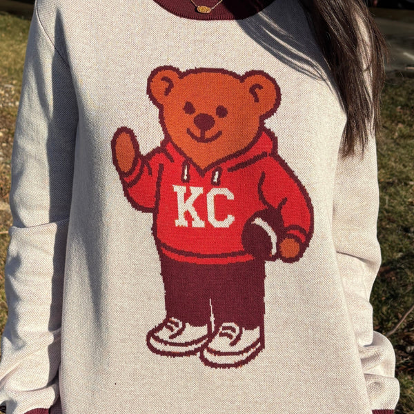 Sweater with a bear graphic wearing a red 'KC' hoodie, standing outdoors.