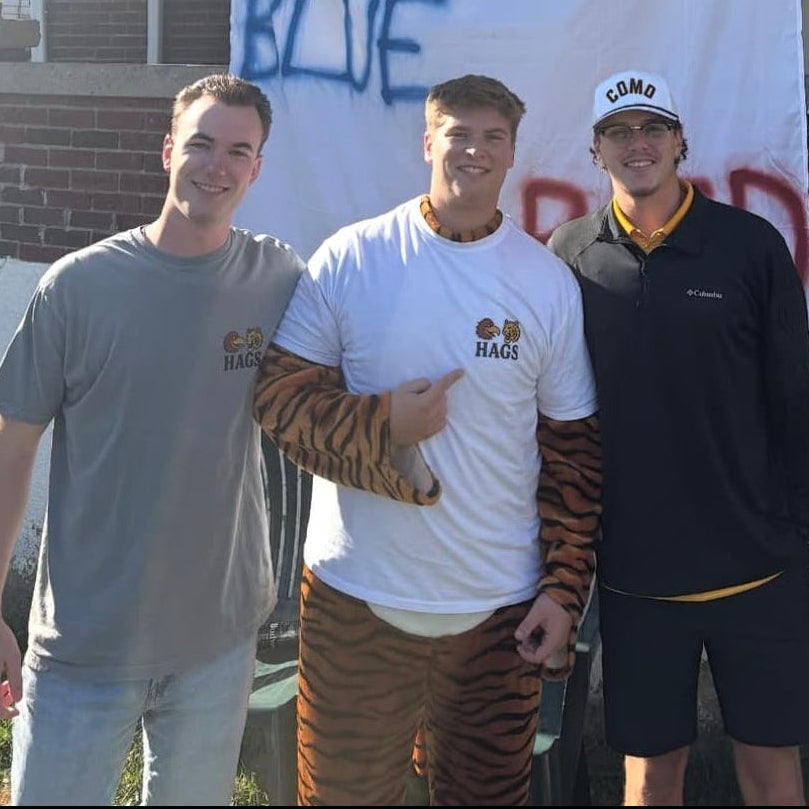 Three men standing in front of a banner with anti-blue sentiment, with a house in the background.