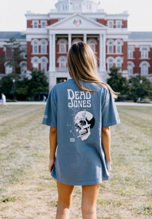 Woman wearing the blue-gray HAGS Dead Jones Band skull T-shirt, showing the white skull back graphic.