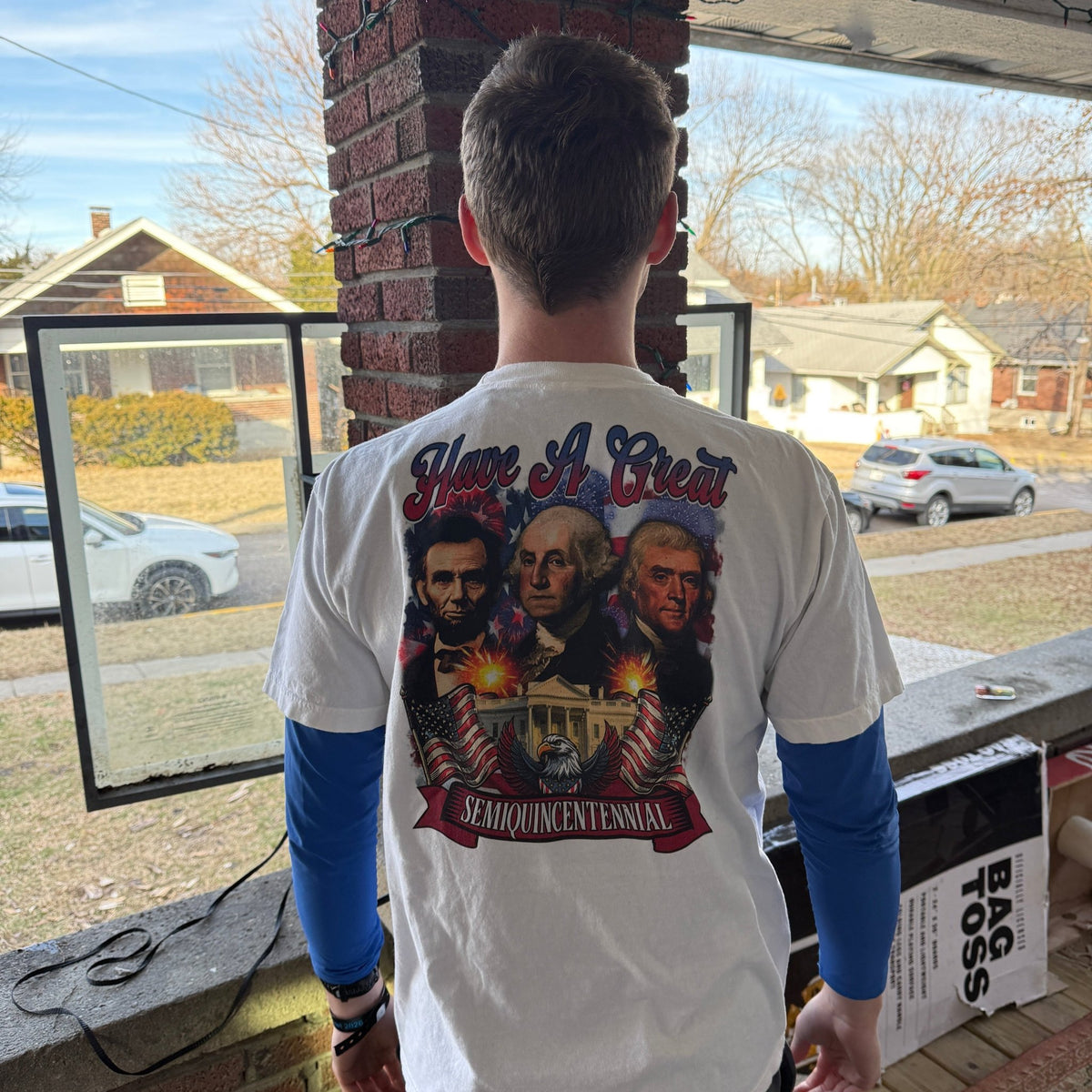 Back view of a man wearing the white HAGS Have a Great Semiquincentennial T-shirt with a patriotic portrait collage.